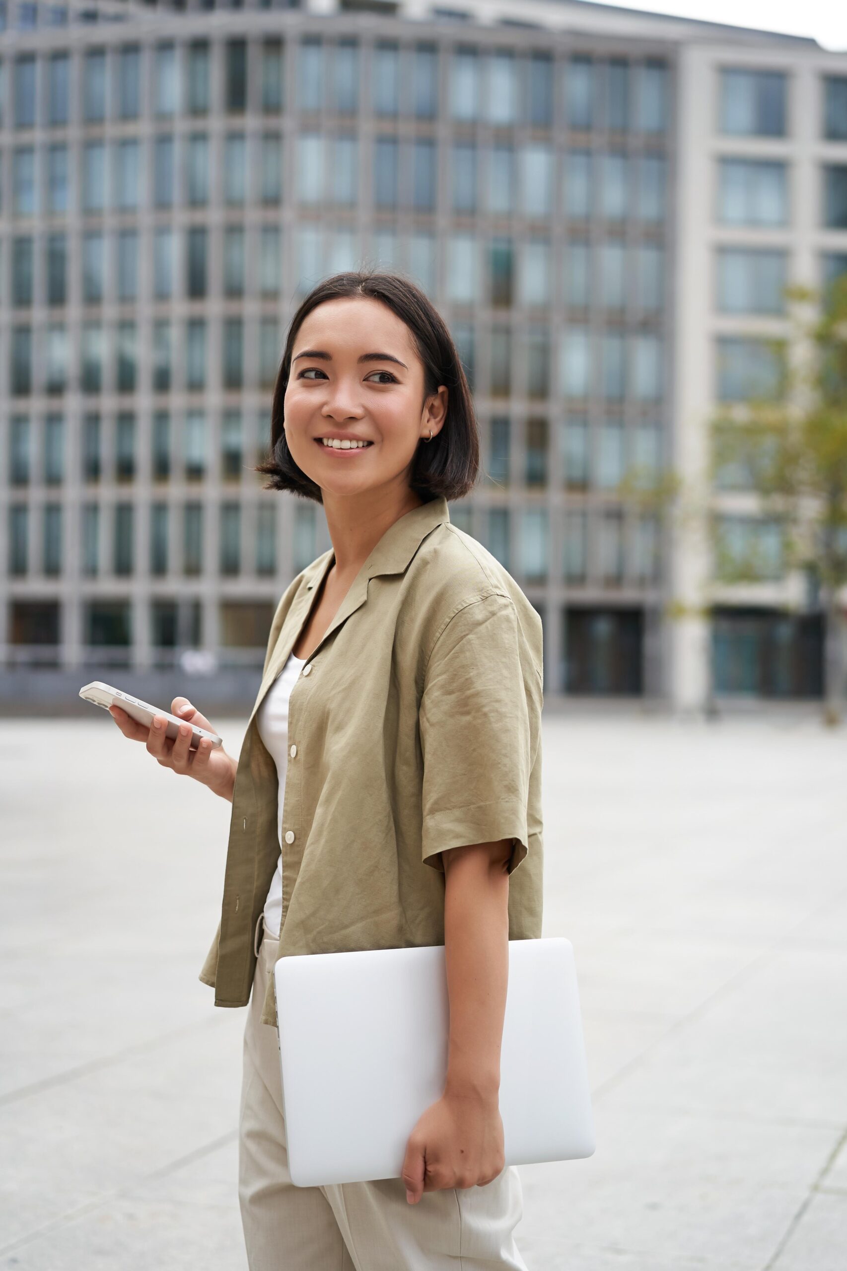 vertical-shot-asian-girl-walks-with-laptop-city-street-smiles (1)